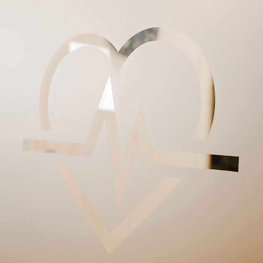 Das Logo bestehend aus einem Herz mit EKG-Kurve auf einer Glaswand